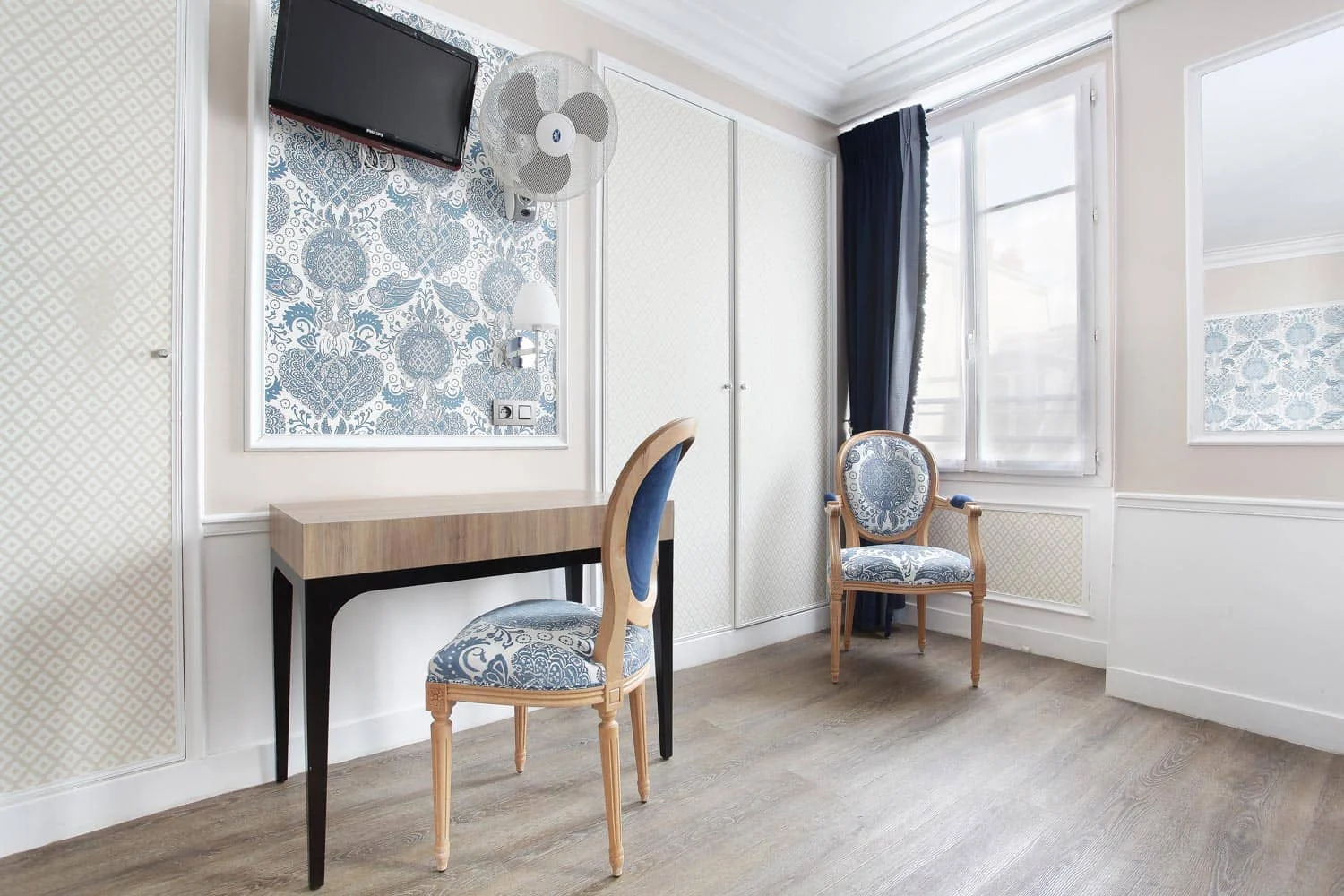 Coin bureau avec chaise médaillon en tissu bleu, télévision murale et fenêtre aux rideaux bleu nuit