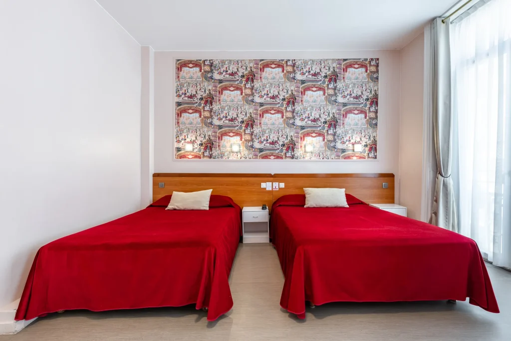 Chambre spacieuse avec deux grands lits aux couvre-lits rouges et panneau mural inspiré du théâtre
