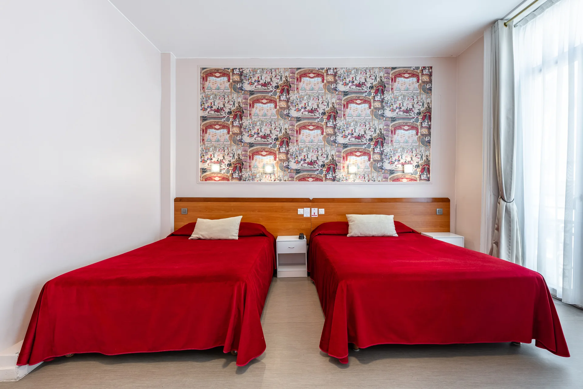 Chambre spacieuse avec deux grands lits aux couvre-lits rouges et panneau mural inspiré du théâtre
