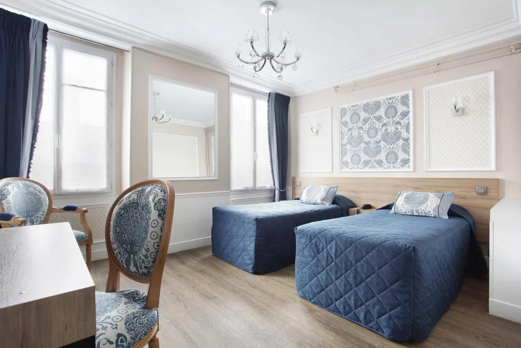 Chambre twin avec deux lits simples aux couvre-lits bleus matelassés, lustre et deux fenêtres