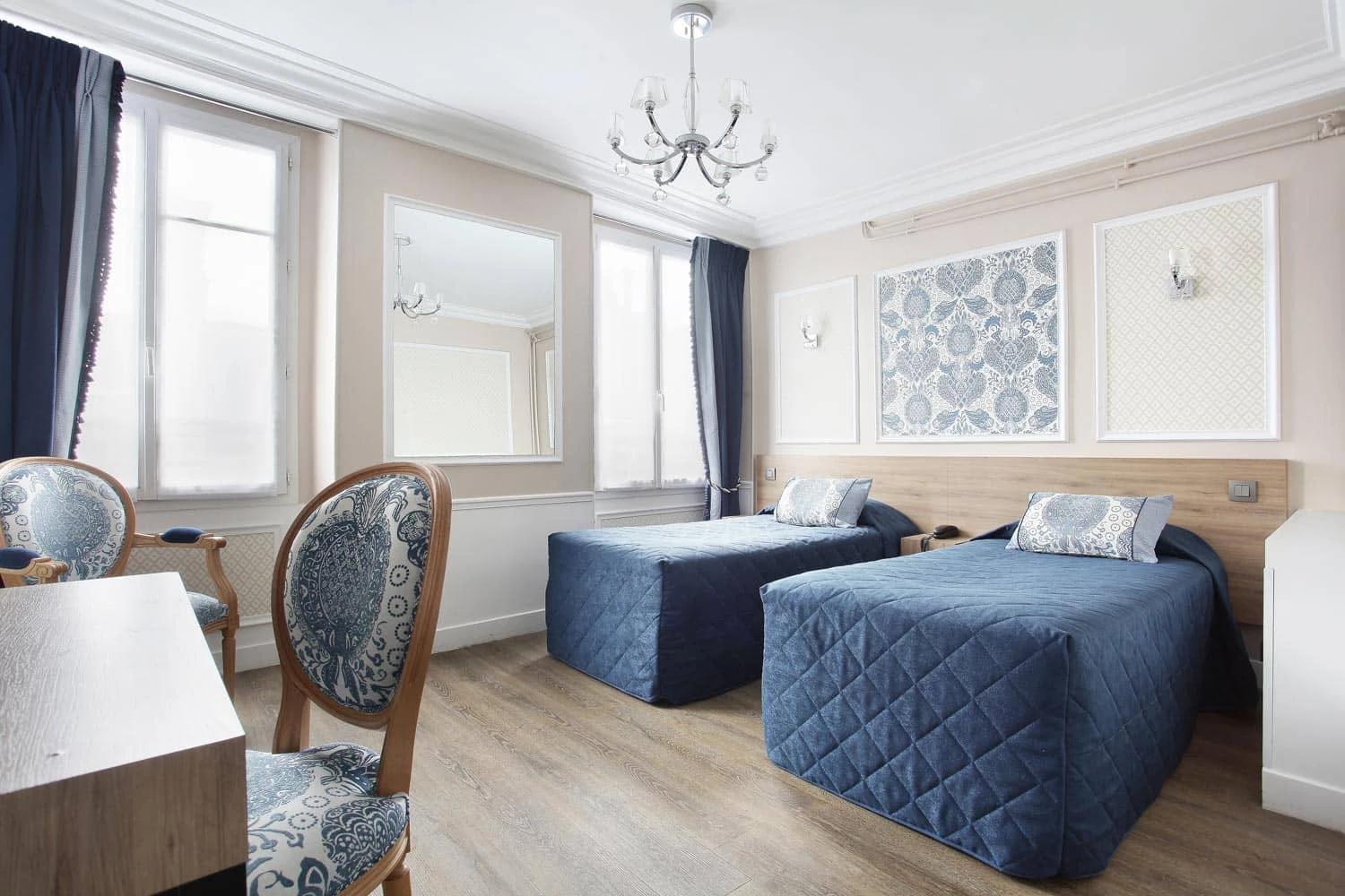 Chambre twin avec deux lits simples aux couvre-lits bleus matelassés, lustre et deux fenêtres