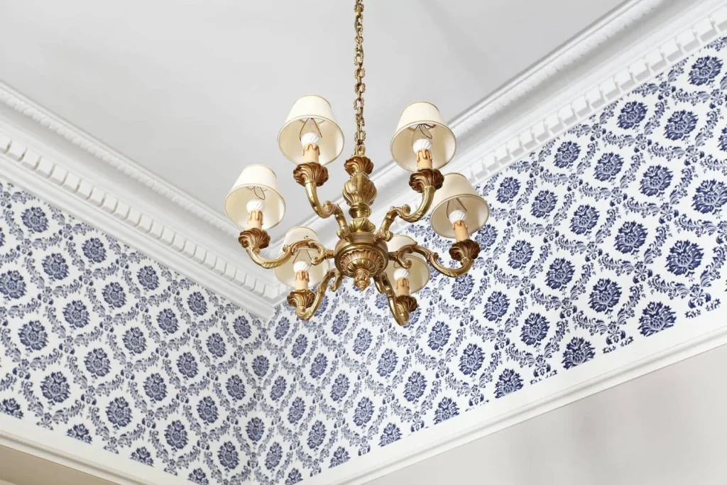 Lustre doré à abat-jour blancs sous une corniche moulurée, papier peint à motifs bleus