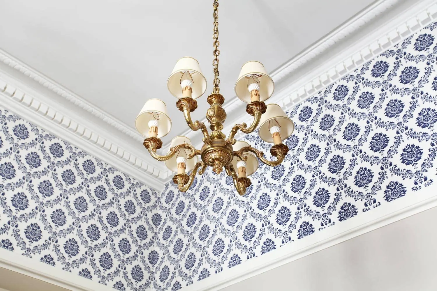 Lustre doré à abat-jour blancs sous une corniche moulurée, papier peint à motifs bleus
