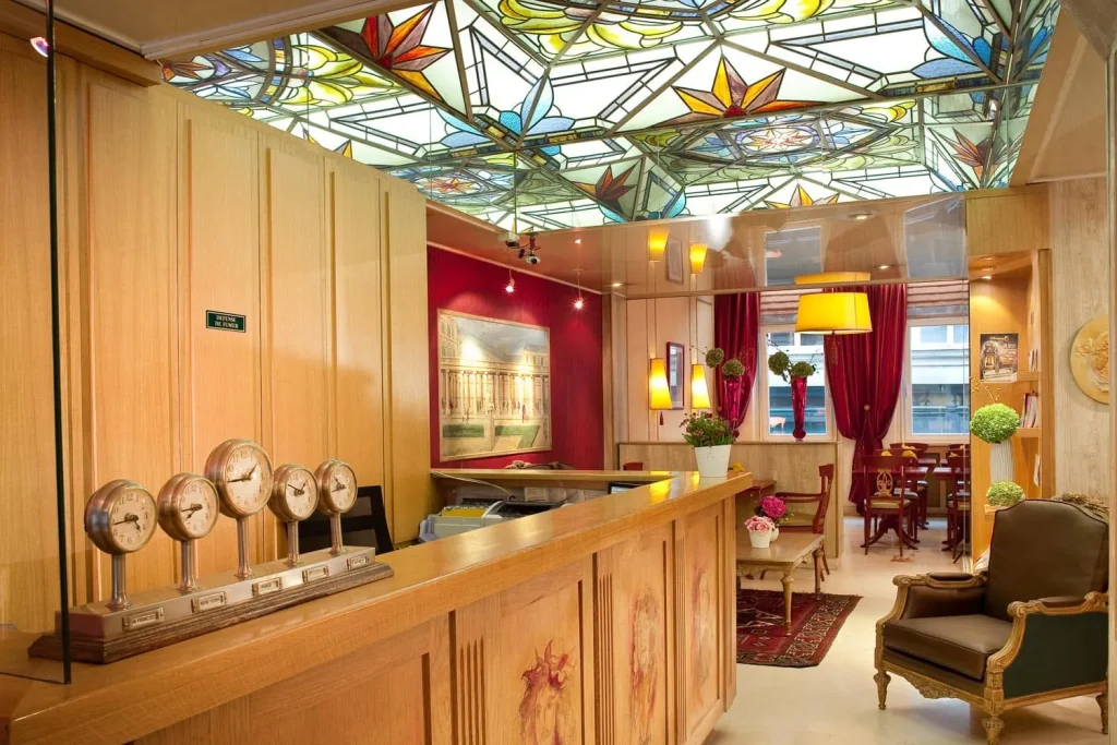 Hall de l'hôtel avec comptoir de réception, horloges anciennes et verrière en vitrail