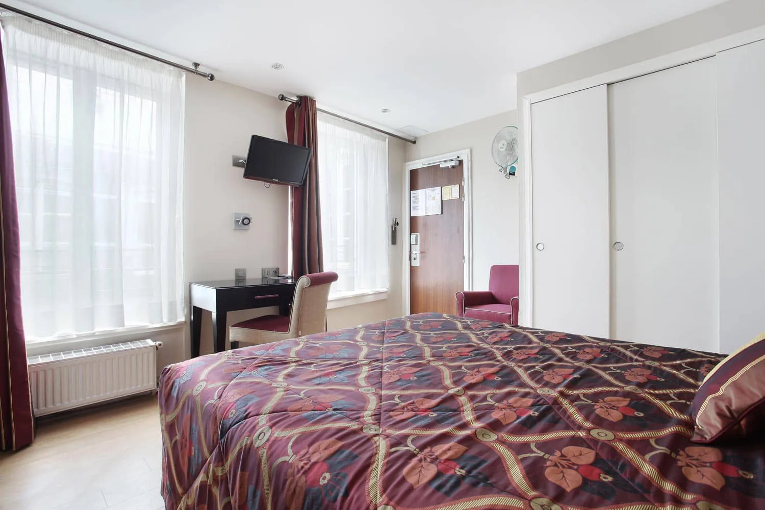 Chambre double vue depuis le lit, avec bureau, télévision et fenêtres voilées de blanc