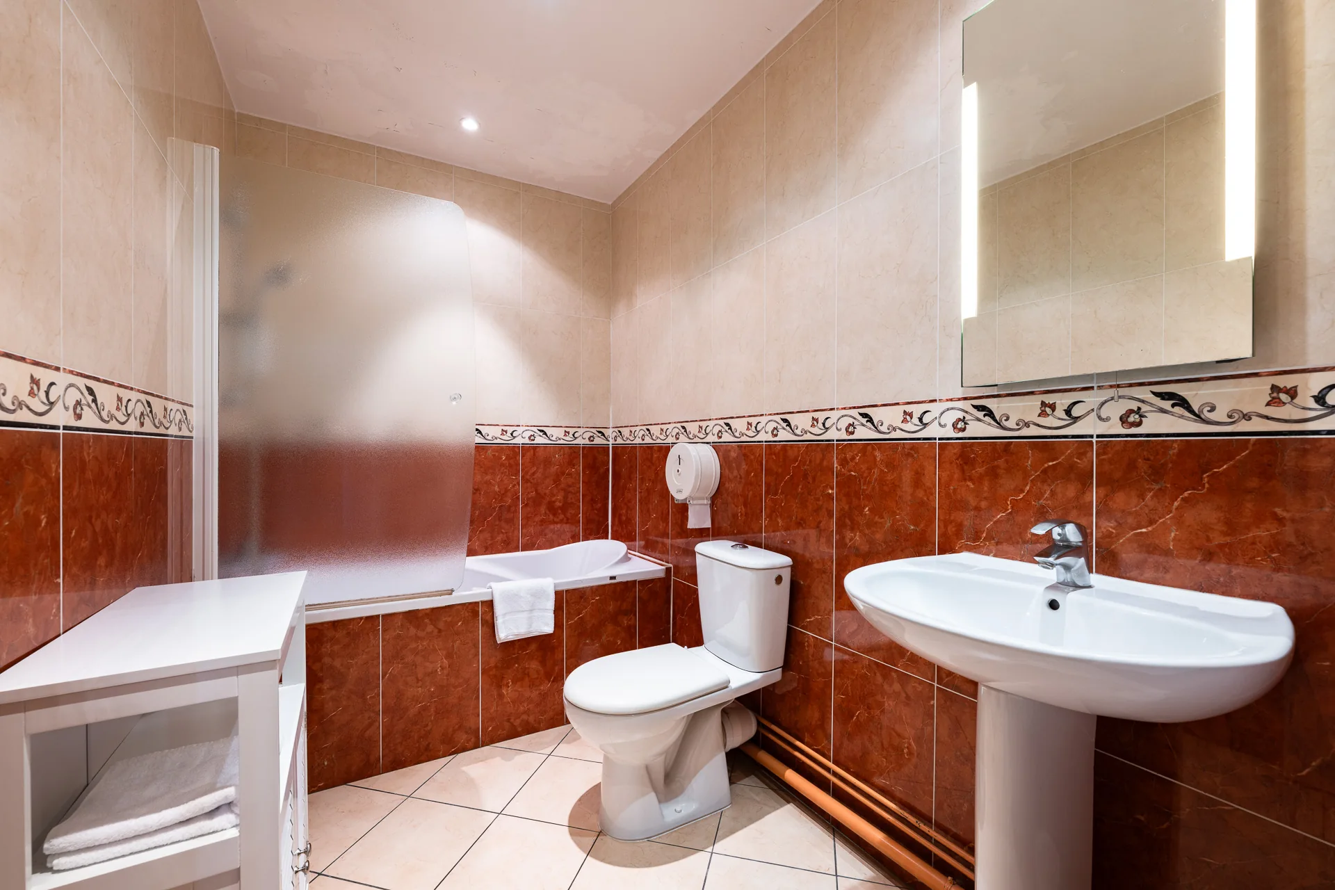Salle de bains avec baignoire, lavabo sur colonne et carrelage rouge brique à frise