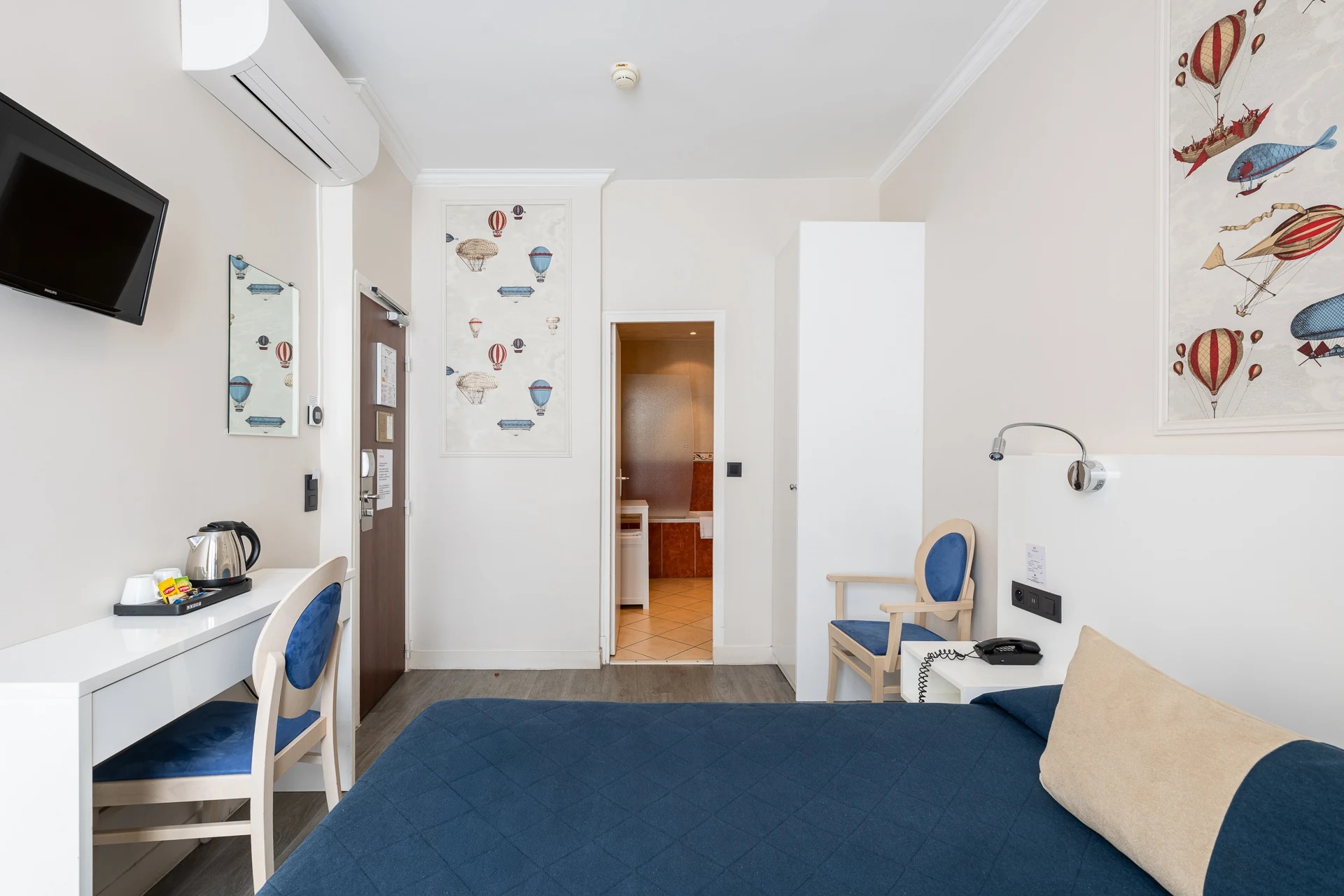 Chambre double avec couvre-lit bleu marine, bureau blanc, bouilloire et télévision