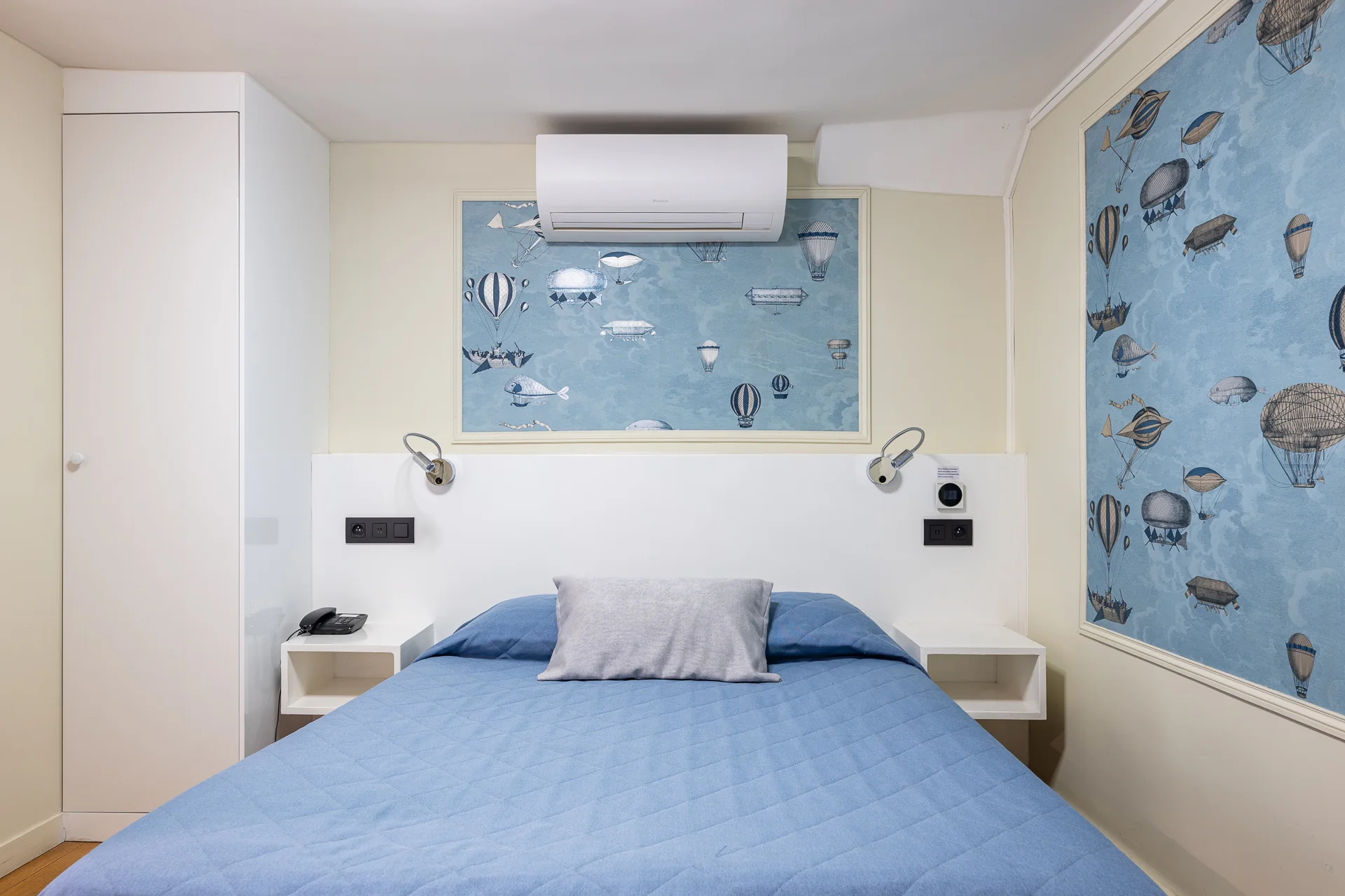 Chambre avec couvre-lit bleu, liseuses et panneaux de montgolfières sur fond bleu