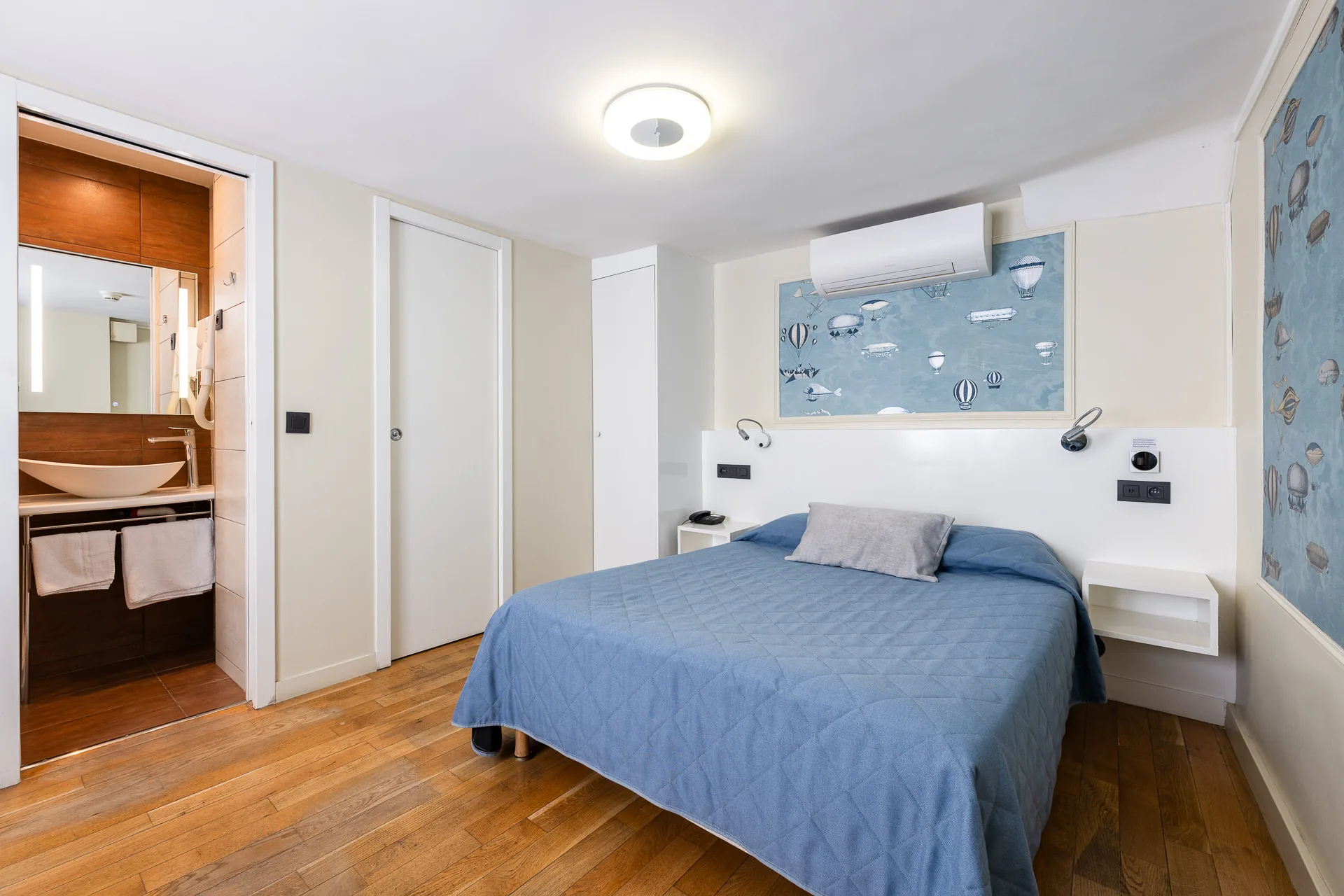 Chambre au parquet en bois, lit au couvre-lit bleu et salle de bains ouverte