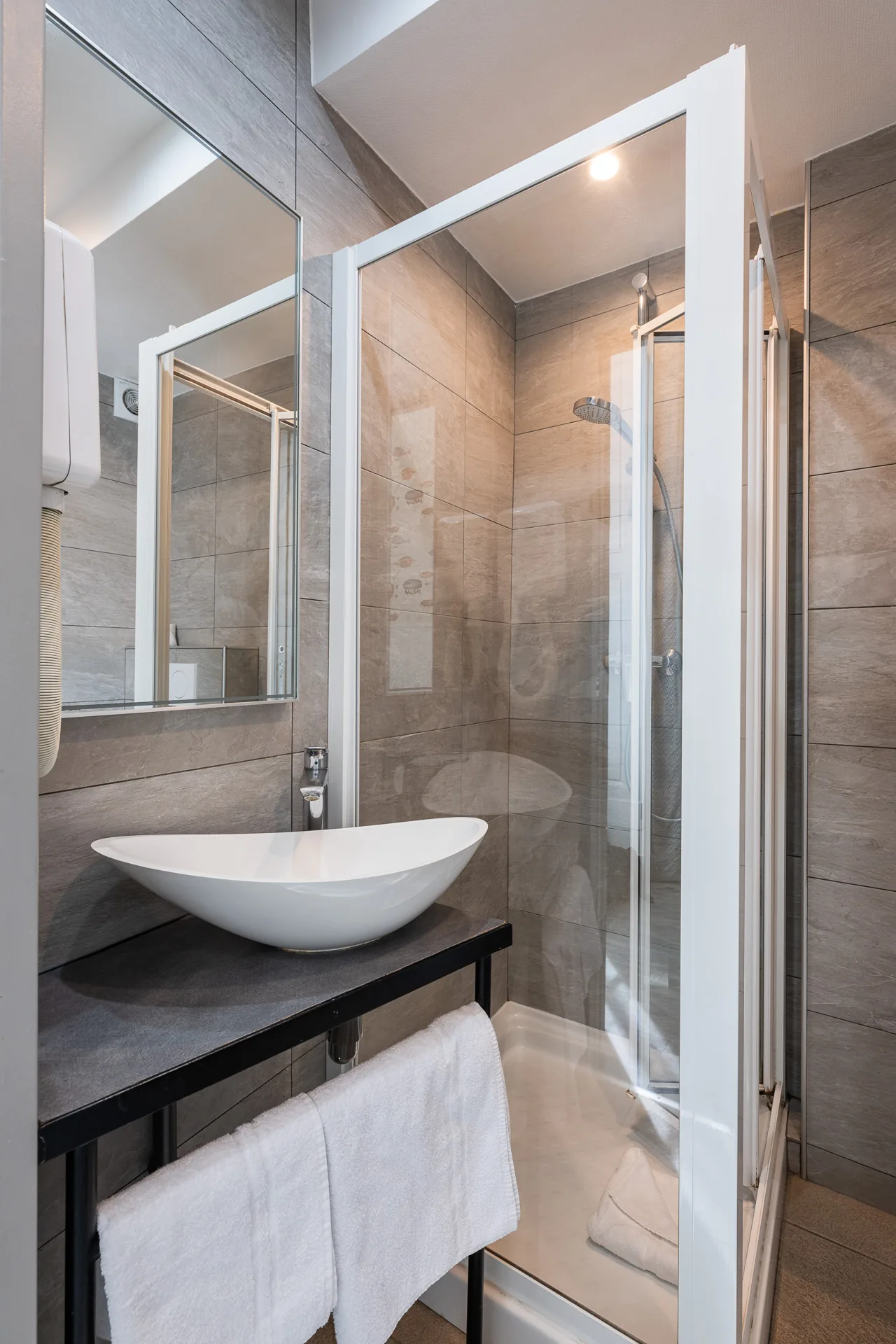 Salle de douche avec vasque blanche, cabine vitrée et serviettes pliées