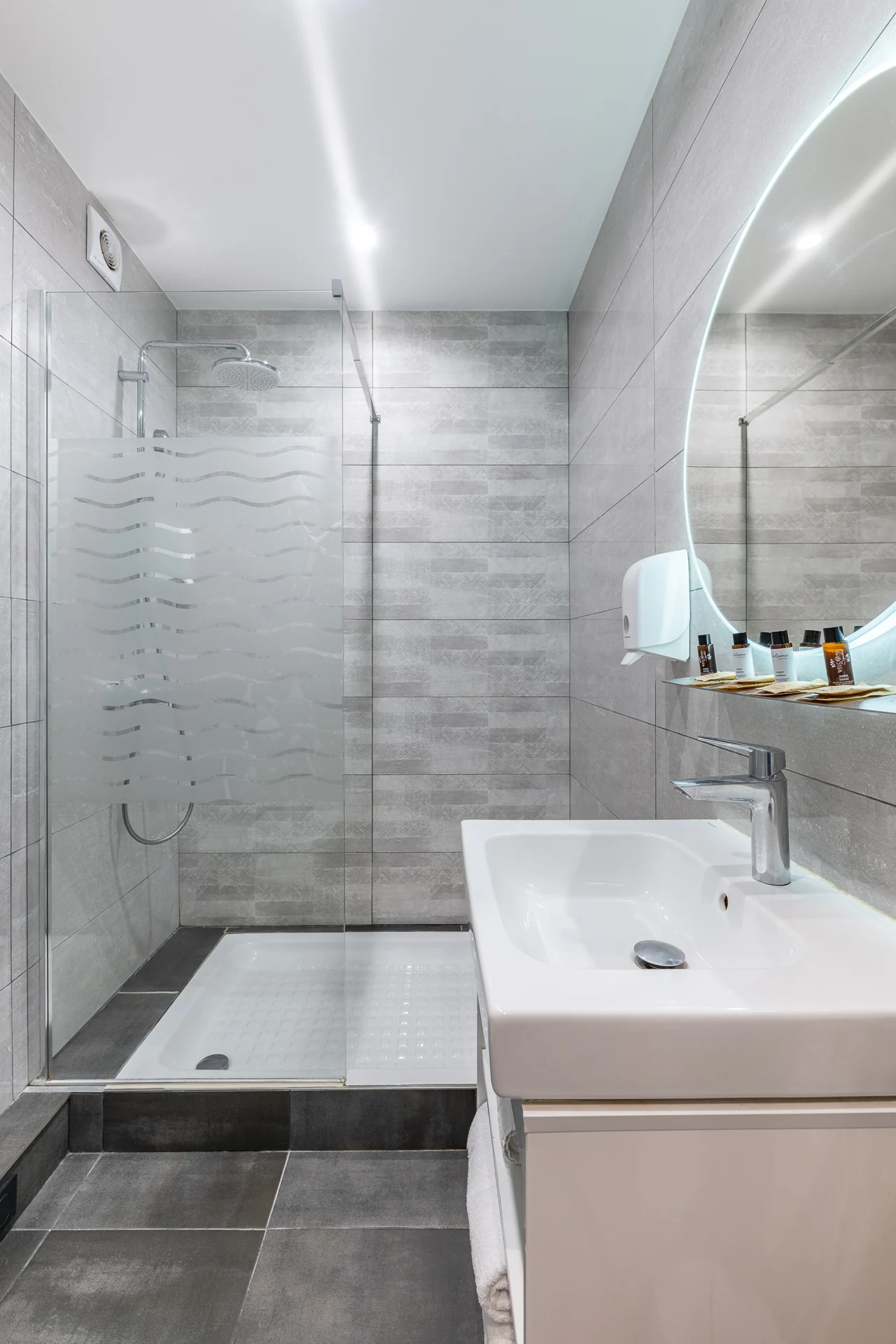 Douche à l'italienne avec paroi vitrée, vasque blanche et miroir rond lumineux