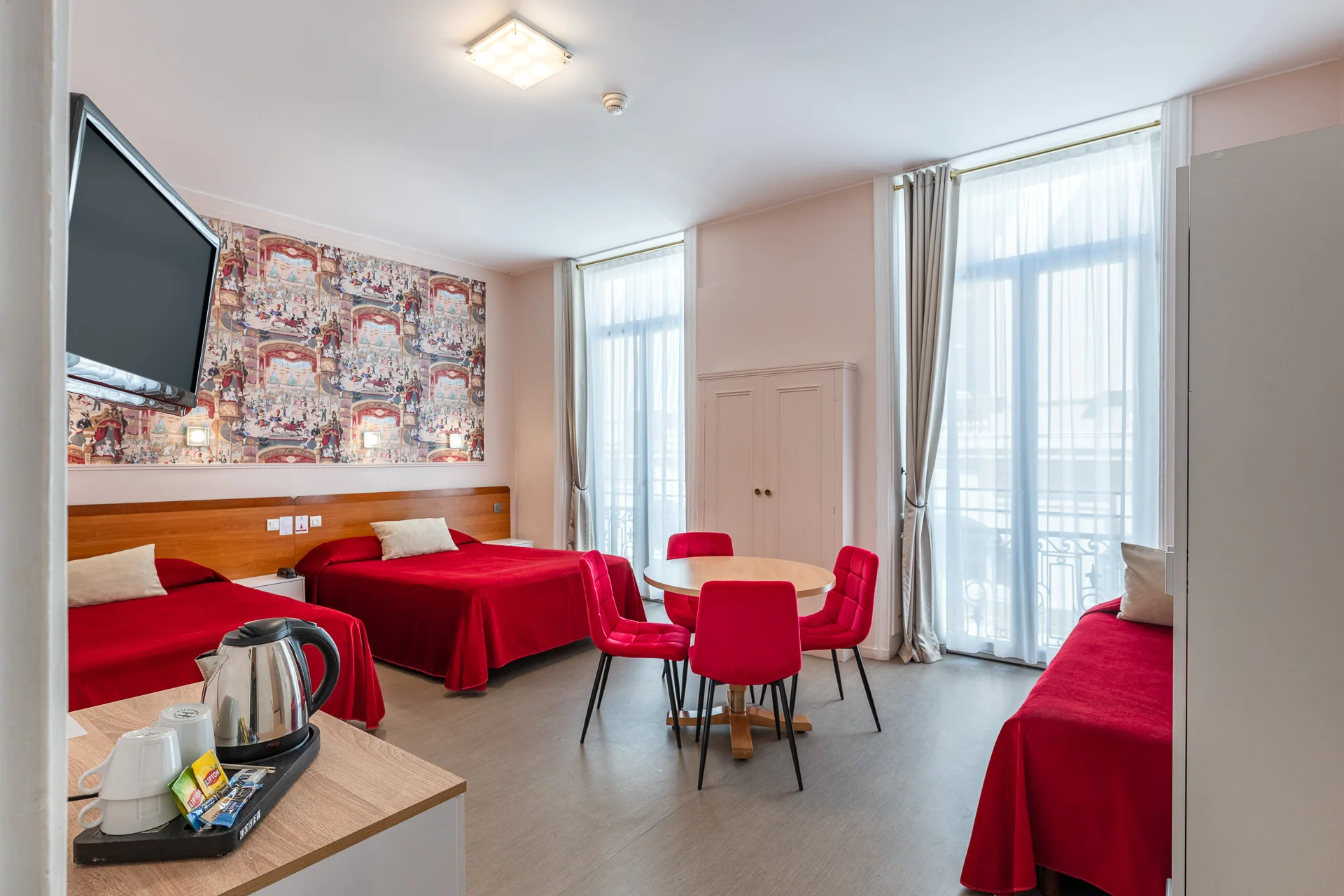 Chambre triple avec trois lits rouges, table ronde, télévision et bouilloire