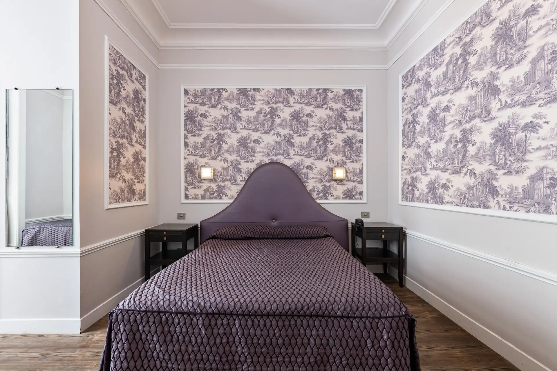 Lit double à tête de lit mauve entre deux tables de chevet, murs en toile de Jouy