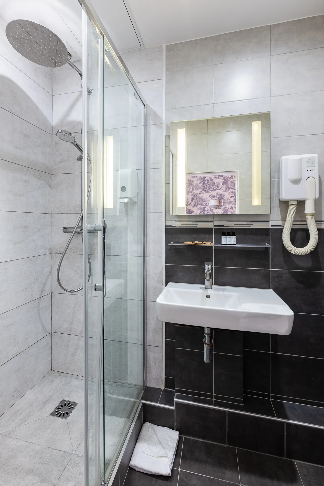 Cabine de douche vitrée, lavabo suspendu et miroir lumineux dans une salle de douche grise