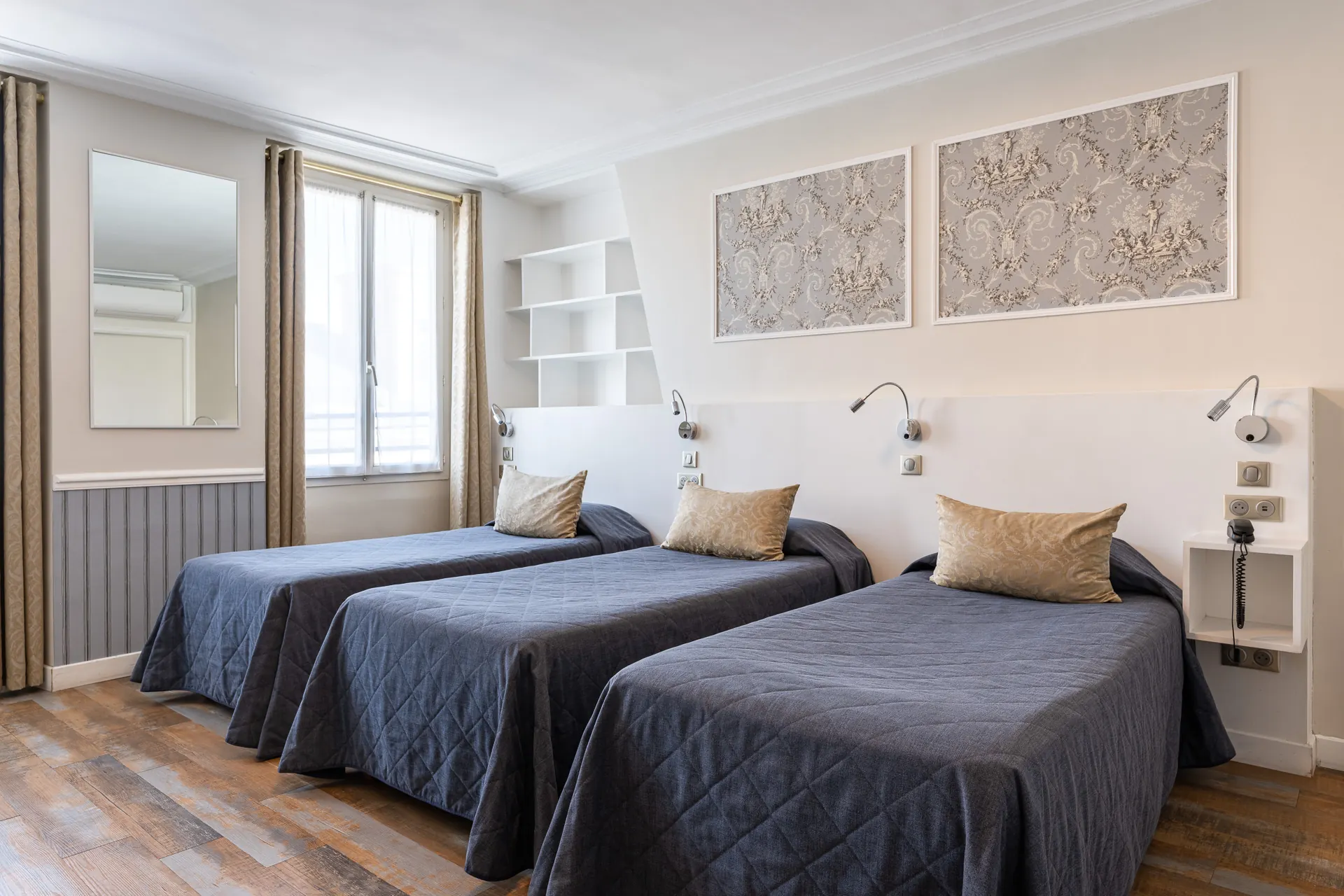 Chambre triple avec trois lits simples aux couvre-lits bleu nuit, tête de lit blanche et toile de Jouy encadrée