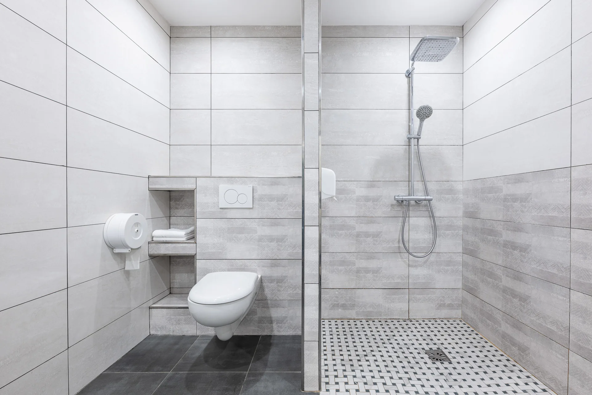 Douche à l'italienne avec pommeau pluie, sol en mosaïque et WC suspendu dans une salle de bains grise