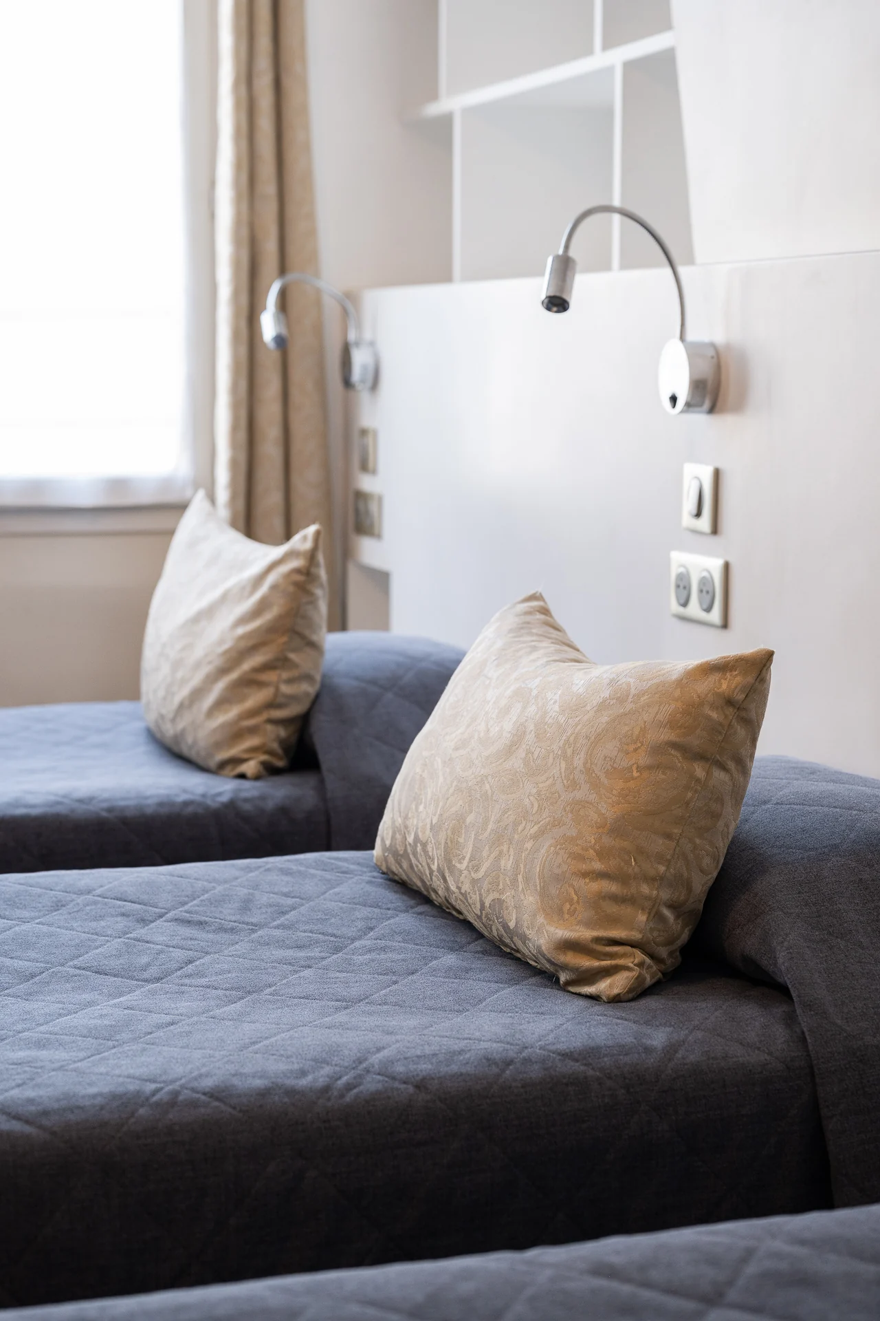 Coussins dorés sur des lits aux couvre-lits bleu nuit, liseuses chromées sur la tête de lit