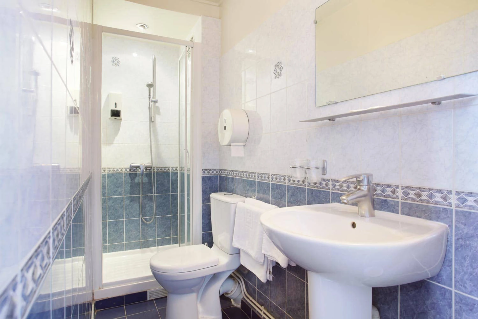Salle de douche avec cabine vitrée, WC et lavabo, carrelage bleu et blanc