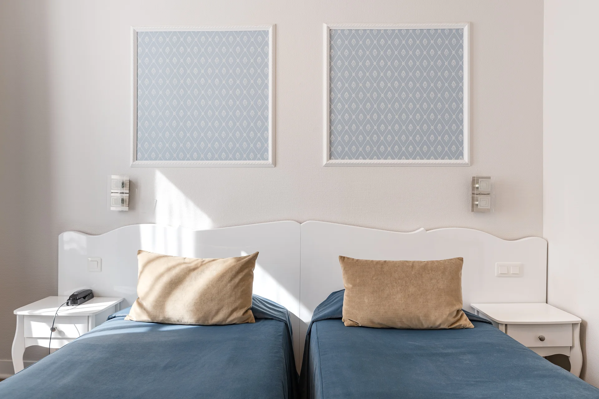 Deux lits simples aux couvre-lits bleus et coussins beiges, têtes de lit blanches et papier peint bleu encadré
