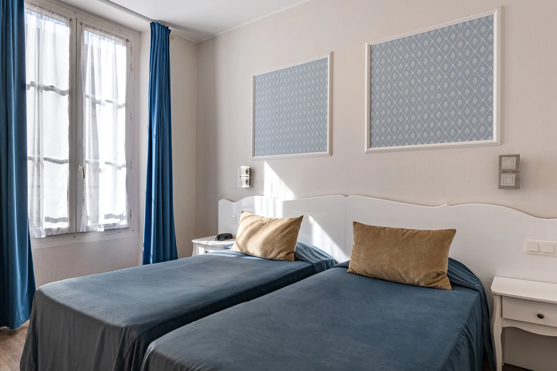 Chambre twin avec fenêtre aux rideaux bleus et deux lits simples baignés de soleil