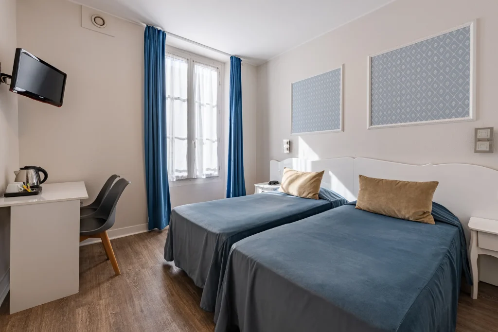 Chambre twin avec bureau blanc, bouilloire, télévision murale et deux lits simples