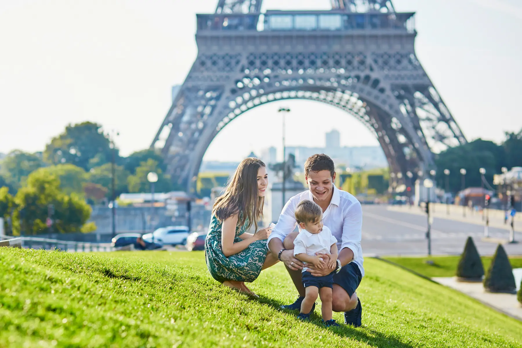 Parents et jeune enfant assis sur une pelouse devant la tour Eiffel